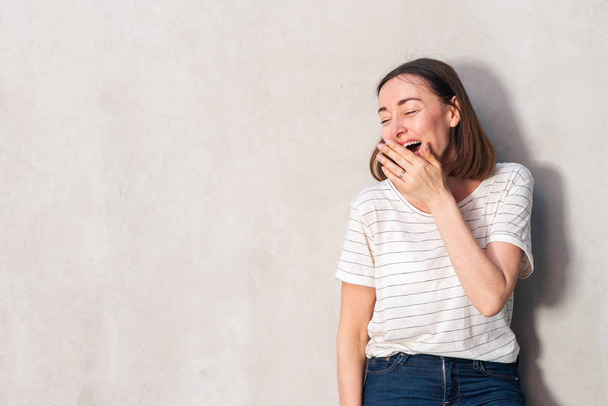 Portrait of beautiful middle aged woman laughing with hand over mouth by white wall - Fotoğraf, Görsel