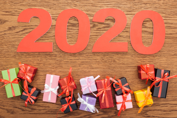bovenaanzicht van papieren 2020 nummers bij kleine decoratieve geschenkdoosjes op houten ondergrond - Foto, afbeelding