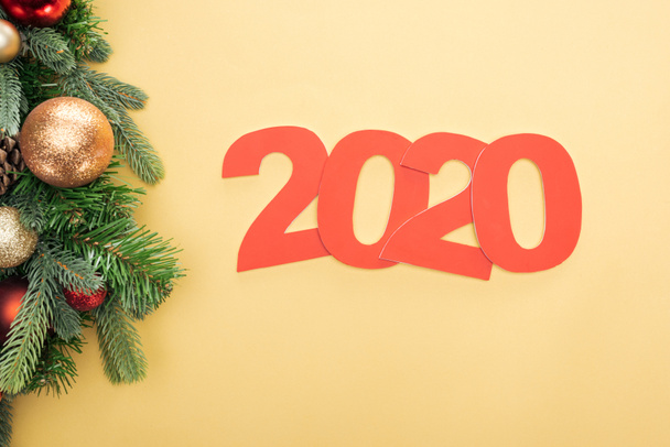top view of paper 2020 numbers near christmas tree branch with baubles on yellow background - Фото, зображення