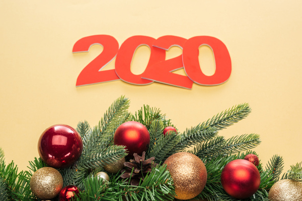 paper 2020 numbers near christmas tree branch with baubles on yellow background - Fotó, kép