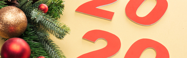 panoramic shot of paper 2020 numbers near christmas tree branch with baubles on yellow background - 写真・画像
