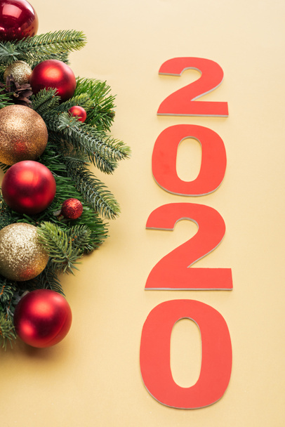 red 2020 numbers near christmas tree branch with baubles on yellow background - Foto, imagen