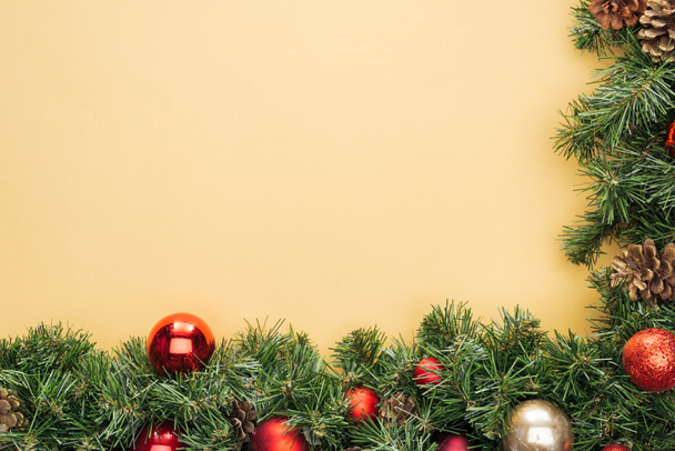 top view of christmas tree branch with red and golden baubles on yellow background - Fotografie, Obrázek