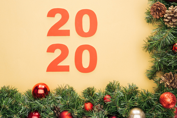 Draufsicht auf Papier 2020 Zahlen in der Nähe von Weihnachtsbaum Zweig mit Kugeln auf gelbem Hintergrund - Foto, Bild