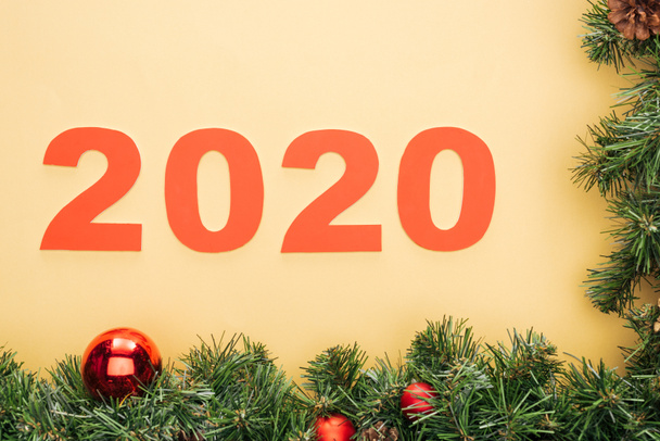 top view of paper 2020 numbers near christmas tree branch with baubles on yellow background - Foto, Bild