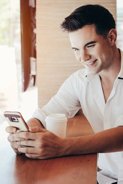 Smart young caucasian businessman using smartphone and drinking  - Photo, Image