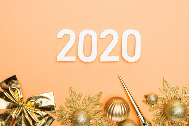 オレンジ色の背景に白い2020年の数字と黄金のクリスマスの装飾のトップビュー - 写真・画像