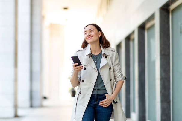 Portrait of smiling older woman walking with cellphone outside - Zdjęcie, obraz