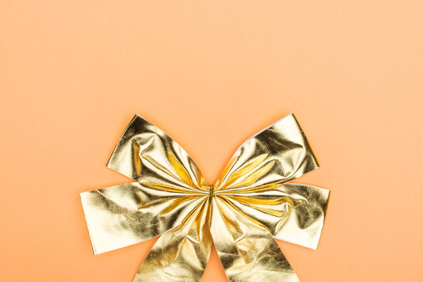 top view of golden shiny decorative bow on orange background with copy space - Fotó, kép