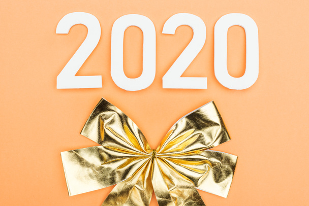 top view of white 2020 numbers near golden bow on orange background - 写真・画像