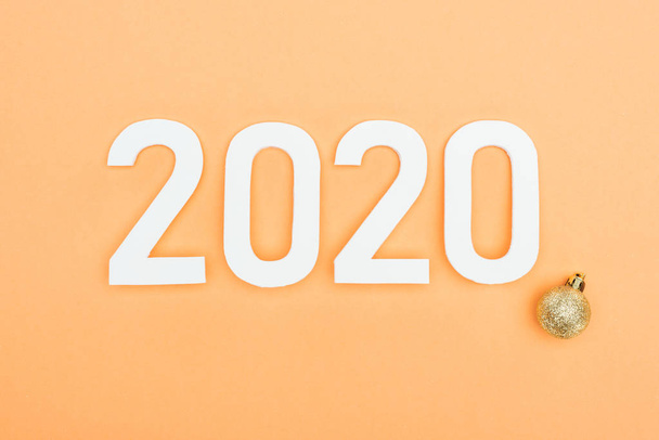 vista superior de números blancos 2020 cerca de adornos de navidad dorados sobre fondo naranja
 - Foto, imagen
