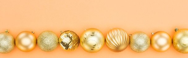 top view of golden christmas baubles in row on orange background, panoramic shot - Photo, image