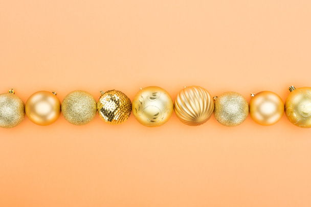 top view of golden christmas baubles in row on orange background - 写真・画像