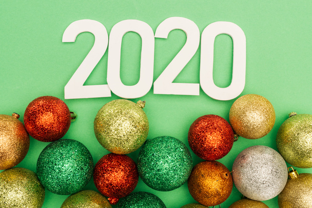 緑色の背景にある多色のクリスマス・ボーブルの近くの白い2020年の数字のトップビュー - 写真・画像