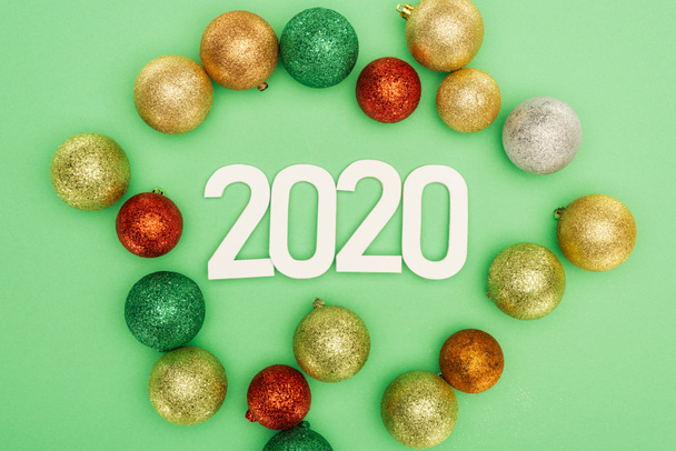 top view of white 2020 numbers near multicolored Christmas baubles on green background - Photo, Image