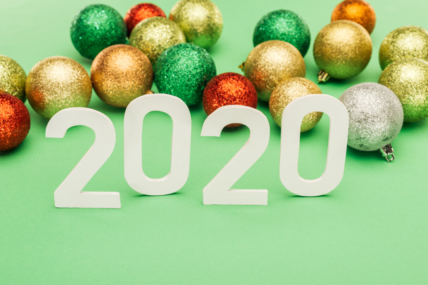 white 2020 numbers near multicolored Christmas baubles on green background - Фото, зображення