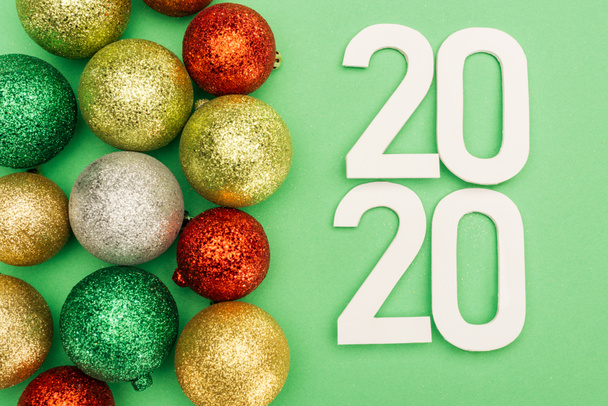 top view of white 2020 numbers near multicolored Christmas baubles on green background - 写真・画像