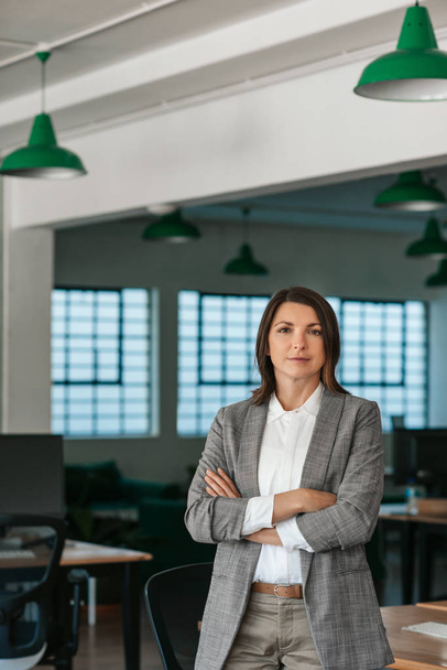 Portrait of a confident businesswoman standing with her arms crossed in a large modern office in the late afternoon - Photo, Image