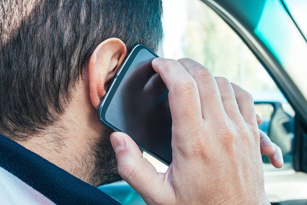Vista de cerca de un hombre sosteniendo un teléfono móvil cerca de su oído y hablando en él mientras conduce. Peligro de usar el teléfono en un coche
 - Foto, Imagen