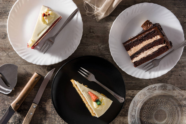 Sortiment sladkých plátků dortu. Čokoláda, mrkev a sametové plátky dortů na dřevěném stole. Horní pohled - Fotografie, Obrázek