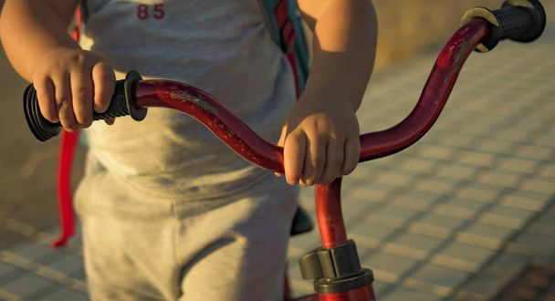 Mały chłopiec bawi się o zachodzie słońca na czerwonym rowerze podczas nauki jazdy. - Zdjęcie, obraz