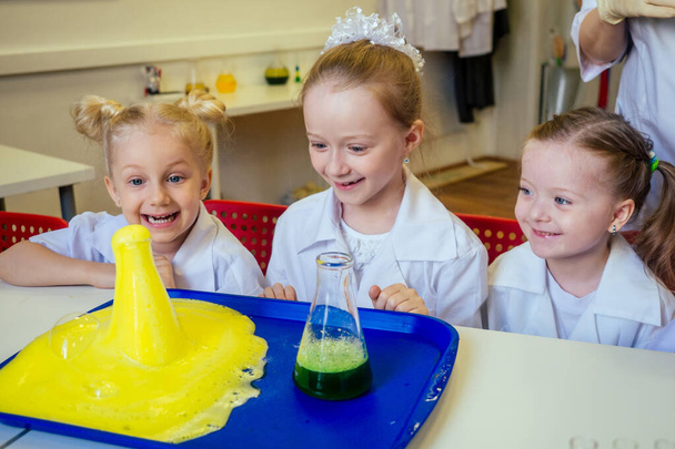 group of school girl kids with teacher in school laboratory making experiment observing the chemical reaction with the dye with vinegar and soda volcano wearing white gown uniform glass - Foto, Imagem