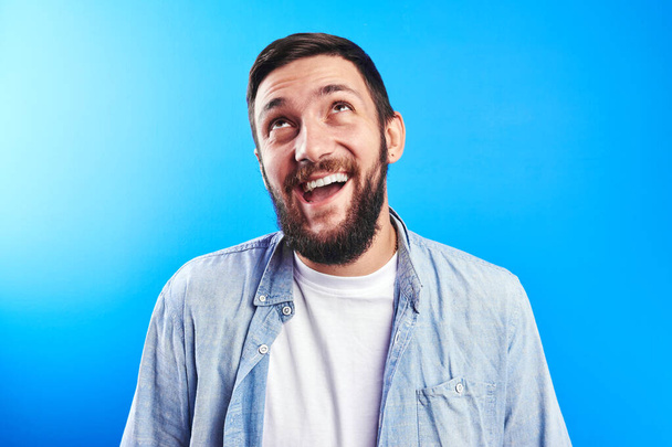 Portrait of toothy smiling and joyfully laughing handsome caucasian brutal bearded man dressed in casual isolated on blue background - Fotografie, Obrázek