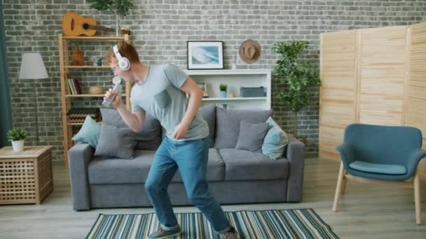 Slow motion of young man dancing in headphones singing in remote control at home - Filmmaterial, Video