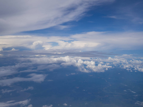 Felhők a kék égbolttal és magas szögletű talajjal rendelkező repülőgép ablakából - Fotó, kép