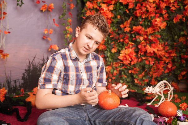 Foto de un joven enojado en Halloween con camisa a cuadros clásica sosteniendo calabaza naranja sobre el fondo de la calle con hojas de otoño
 - Foto, Imagen