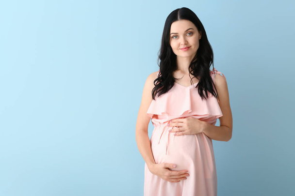 Mooie jonge zwangere vrouw op kleur achtergrond - Foto, afbeelding