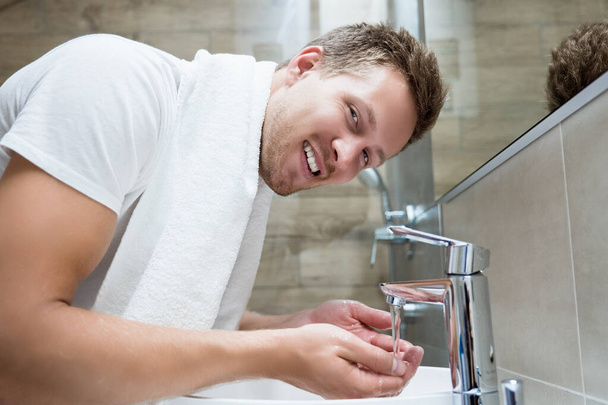 Genç yakışıklı adam banyoda yüzünü yıkıyor. - Fotoğraf, Görsel
