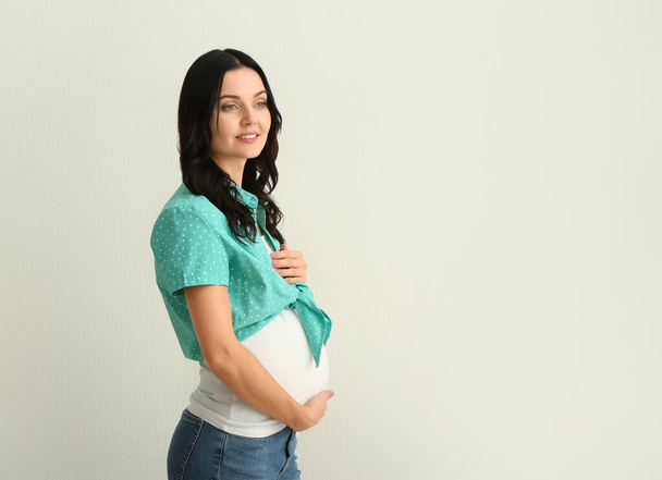 Krásná mladá těhotná žena na světlé pozadí - Fotografie, Obrázek