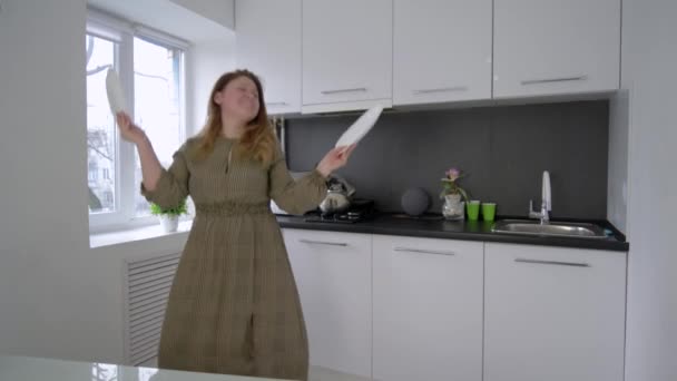 crazy happy housewife having fun and sings with dishes in arms at kitchen at home - Video, Çekim