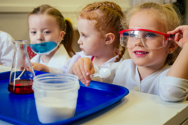 group of school girl kids with teacher in school laboratory making experiment observing the chemical reaction with the dye with vinegar and soda volcano wearing white gown uniform glass - Foto, Imagem