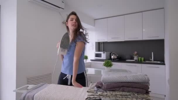 Hausarbeit, lustige Haushälterin mit eisernem Tuch am Bügelbrett und Spaß beim Tanzen und Singen - Filmmaterial, Video