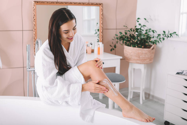 Beautiful young woman applying cream on her legs in bathroom - Foto, Bild