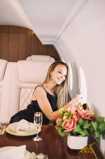 beautiful young girl in the cabin of a business class airplane with a phone in her hands comfortable luxury travel close to the porthole - Foto, Bild