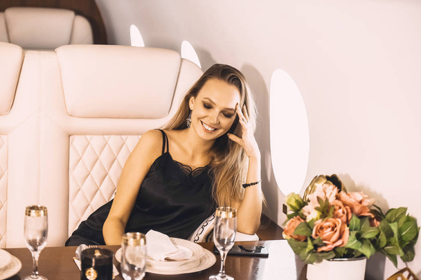 beautiful young girl in the cabin of a business class airplane with a phone in her hands comfortable luxury travel close to the porthole - Fotografie, Obrázek