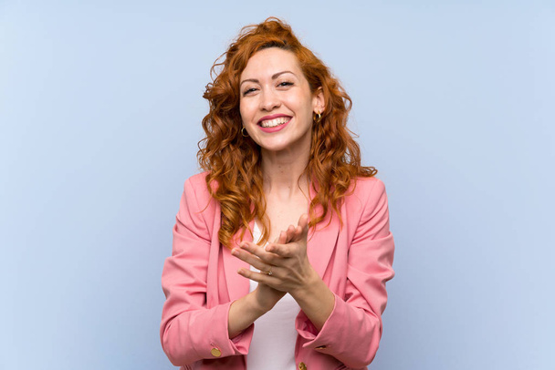 Redhead woman in suit over isolated blue wall applauding after presentation in a conference - Photo, Image