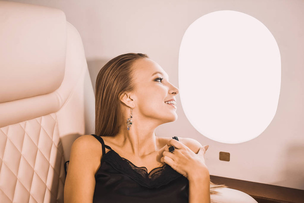 beautiful young girl in the cabin of a business class airplane with a phone in her hands comfortable luxury travel close to the porthole - Foto, Imagem