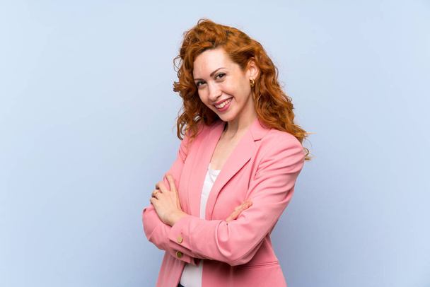 Redhead woman in suit over isolated blue wall with arms crossed and looking forward - Photo, Image