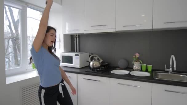 szczęśliwy śmieszne gospodyni domowa kobieta wygłupiając się i śpiewa z naczyniami w ramionach w kuchni w domu - Materiał filmowy, wideo