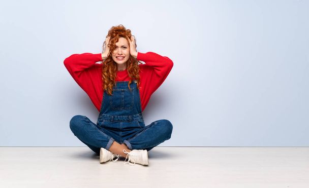 Redhead žena s montérkami sedí na podlaze frustrovaný a bere ruce za hlavu - Fotografie, Obrázek