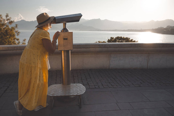Érett női utazó néz keresztül turisztikai távcső a hegyek és a tenger. A nyugdíjasok utazásának fogalma. - Fotó, kép