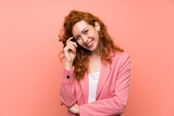 Redhead vrouw in pak over geïsoleerde roze muur lachen - Foto, afbeelding