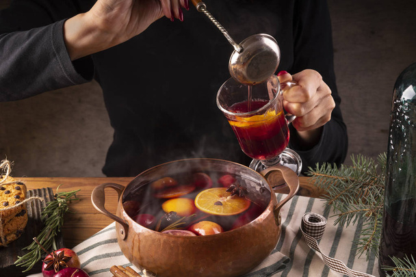 Female hands pour hot mulled wine from a copper pan into a glass. - Fotó, kép
