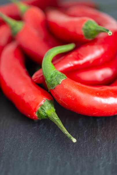 Top view of a close-up of chillies on black slate background, with unfocused background - 写真・画像