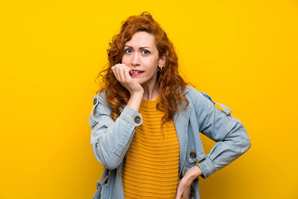 Redhead woman over isolated yellow background nervous and scared - Fotó, kép