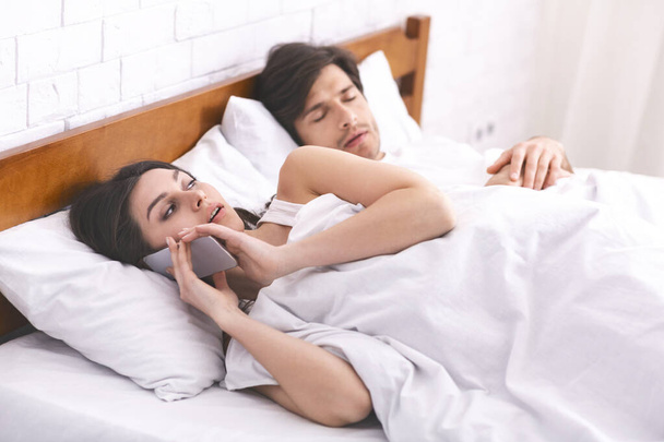 Cheating woman talking privately on cellphone in family bed - 写真・画像